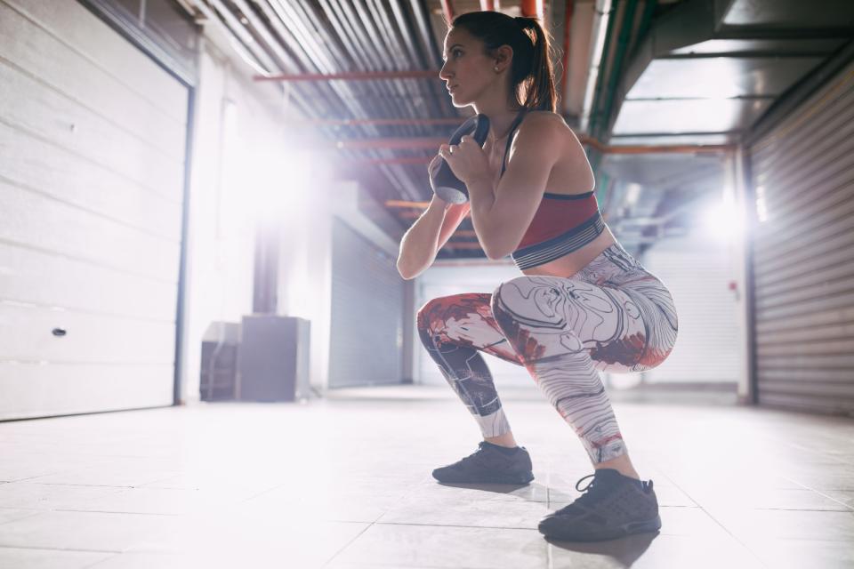 Woman demonstrates a goblet squat with a kettlebell inside of a gym